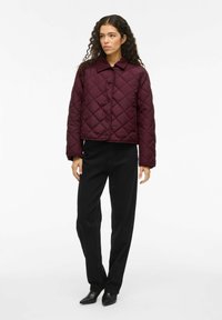 Burgundy quilted jacket with a collar, front buttons, and diamond patterns. Paired with black pants and black pointed shoes.