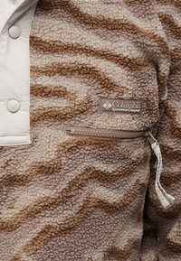 Καφέ και μπεζ fleece μπουφάν με μοτίβο, με τσέπη με φερμουάρ μπροστά και κουμπιά κοντά στον γιακά, με ετικέτα Columbia Sportswear.