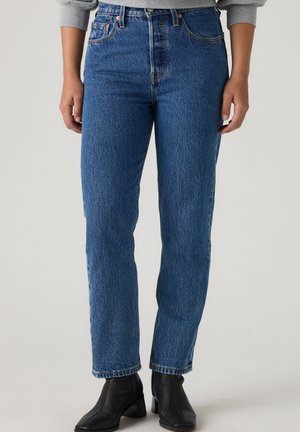 Person som bär raka blå denimjeans med hög midja, kombinerat med svarta kängor och en ljusgrå sweatshirt.