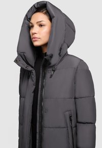 Giubbotto piumino grigio con grande cappuccio, chiusura frontale con zip e tasche laterali. Presenta un design trapuntato con una texture liscia e lucida.