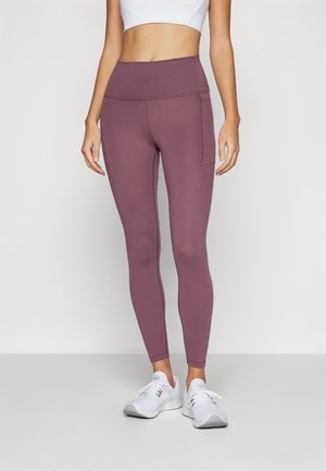 Lilla høytliv leggings med en glatt tekstur, med en sidelomme og en tettsittende design, kombinert med hvite treningssko.