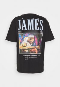 Camiseta negra de manga corta con un gráfico colorido de un jugador de baloncesto, con el texto "KING JAMES" arriba y detalles de Los Ángeles abajo.