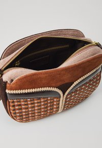 Borsa in suede e pelle marrone con texture intrecciata. Cerniera dorata, tasche interne e bordo cordonato. Vista dall'alto aperta, che mostra la fodera in tessuto.