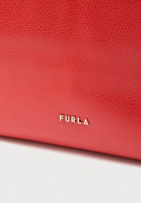 Punainen, teksturoitu nahkalaukku, jossa on kultainen "FURLA"-brändäys. Laukku on sileäpintainen ja siinä on selkeä rungon kuvio. Kompakti ja minimalistinen muotoilu.