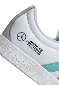 Vita Adidas-sneakers med turkosa ränder, Mercedes-Benz stjärnlogotyp och AMG Petronas Formula One Team-märkning på sidan.