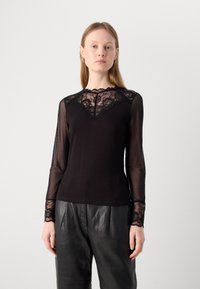 Haut noir à manches longues avec des accents en dentelle au niveau du col et des poignets ; tissu doux en dessous, manches transparentes et silhouette ajustée.