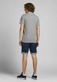 Graues Baumwoll-T-Shirt mit kurzen Ärmeln, kombiniert mit dunkelblauen Jeansshorts. Die Shorts sind an den Säumen umgeschlagen und werden mit schwarzen Sneakers getragen.
