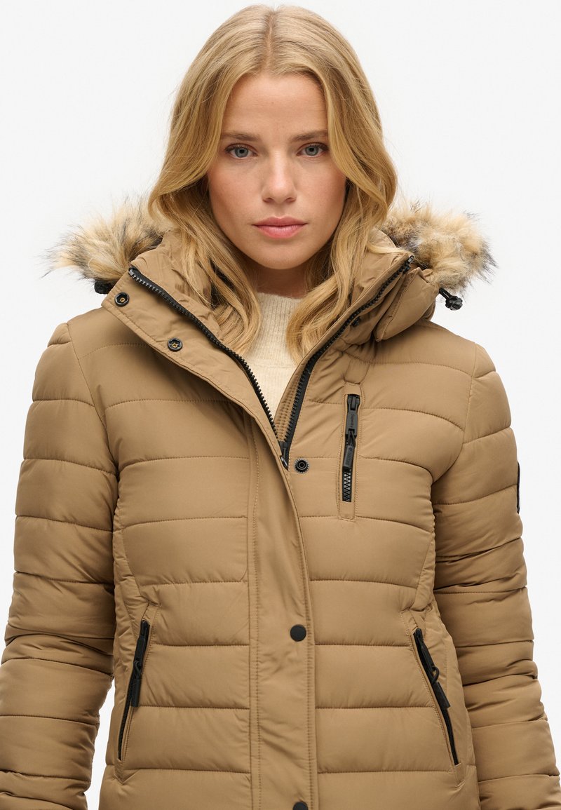 Beige Puffer-Jacke mit abnehmbarem Kunstfell gefüttertem Kapuzen, Reißverschlusstaschen und gestepptem Design. Mit schwarzen Hardware-Akzenten.