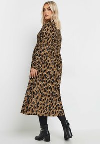 Sukienka midi w panterkę w kolorze brązowym i czarnym, z marszczonym gorsetem i długimi rękawami, zestawiona z czarnymi botkami za kostkę.