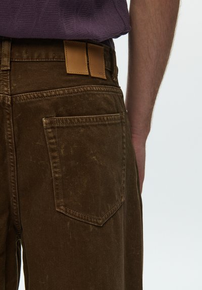 Pantaloni maro din denim cu finisaj texturat, prevăzuți cu o patch de piele la talia din spate și o buzunar posterior cu detalii cusute.