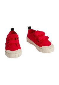 Baskets en tissu rouge avec deux bandes Velcro, bout en caoutchouc blanc et semelle texturée, dotées d'une languette noire au talon.