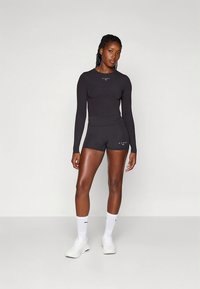 Crni sportski top s dugim rukavima i pripadajuće visokodržavne kratke hlače. Tkanina je glatka; s bijelim naglascima logotipa. Uključene su bijele čarape i cipele.