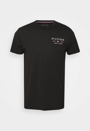 Musta puuvillapaita, jossa on pyöreä kaula-aukko, lyhyet hihat ja valkoinen logo punaisilla yksityiskohdilla, jossa lukee "HILFIGER EST. 1985 NEW YORK."