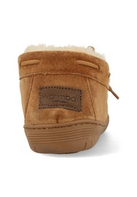 Bruine suède enkellaars met crèmekleurige bontvoering, rubberen zool en een rechthoekig bruin etiket met de merknaam. Subtiele stiksels als accent.