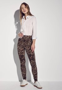 Leggings in stampa leopardata con una texture liscia, abbinati a una camicia bianca a bottoni. Sneakers bianche con accenti marroni completano l'outfit.