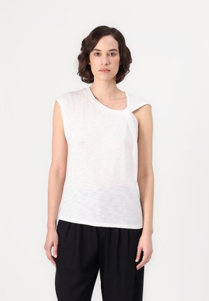 White sleeveless top with a twisted knot detail at the shoulder, made of lightweight fabric. The fit is relaxed, paired with black trousers.