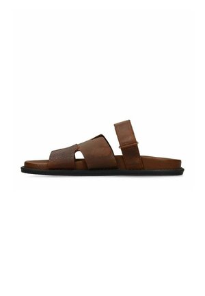 Bruine leren sandalen met twee brede banden en een verstelbare enkelband op een platte zwarte zool, zijaanzicht op witte achtergrond.
