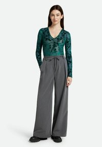 Top de manga larga con estampado floral verde y escote en V, combinado con pantalones de pierna ancha grises de talle alto y zapatos negros de suela gruesa.