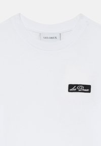 White cotton t-shirt featuring a rounded neckline and a small black embroidered label with "Les Deux" on the left chest.