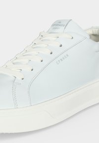 Hvid lædersneaker med hvide snørebånd, "CPNHGN" trykt på siden og "Copenhagen Studios" logo på tungen.