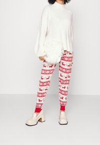 Kremowy sweter dzianinowy z wysokim kołnierzem, zestawiony z legginsami w czerwono-białe wzory z reniferami i geometrycznymi motywami. Kremowe buty na platformie.
