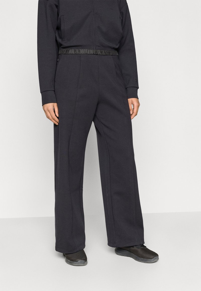 Σκούρα γκρι ολόσωμη φόρμα με υφασμάτινη μαύρη ζώνη στη μέση, μακριά μανίκια και φαρδιά παντελόνια, κατασκευασμένη από μαλακό υλικό με ελάχιστα ραφές.