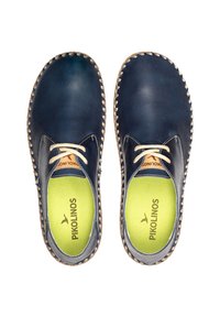 Zapatos de cuero azul marino con punta redonda, cordones color crema y una plantilla verde en contraste que presenta el nombre de la marca "Pikolinos". Bordes cosidos.
