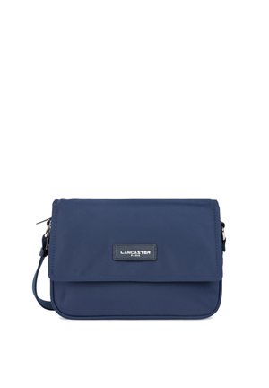 Sac bandoulière en nylon bleu marine avec un rabat, des accessoires en métal argenté et une plaque logo. Forme rectangulaire compacte avec une sangle amovible.