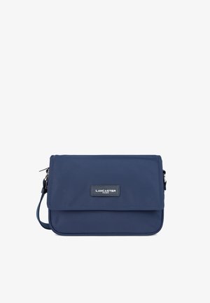 Sac bandoulière en nylon bleu marine avec un rabat, des accessoires en métal argenté et une plaque logo. Forme rectangulaire compacte avec une sangle amovible.