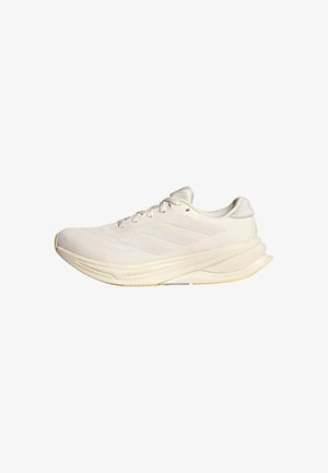 Chaussure de sport beige clair avec une tige en mesh, des lacets plats et une semelle rembourrée. Présente un design à trois bandes sur le côté latéral.