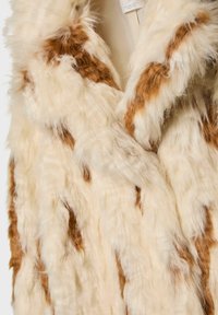 Fuskepelsvest med en cremet base og lysebrune striber. Tæt, blød tekstur med en let glans, med en krave og uden synlige lukninger.