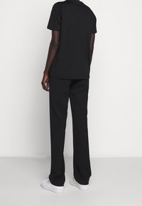 Musta puuvillainen t-paita ja siihen sopivat, rennolla istuvuudella varustetut housut, täydentäen asukokonaisuutta valkoisilla lenkkareilla. Asussa on lyhyet hihat ja yksinkertainen muotoilu.