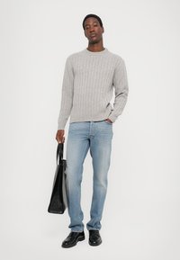 Pulover gri cu striații, blugi bleu deschis, pantofi negri și o geantă tote neagră. Design simplu cu un model texturat de tricot și o croială clasică.