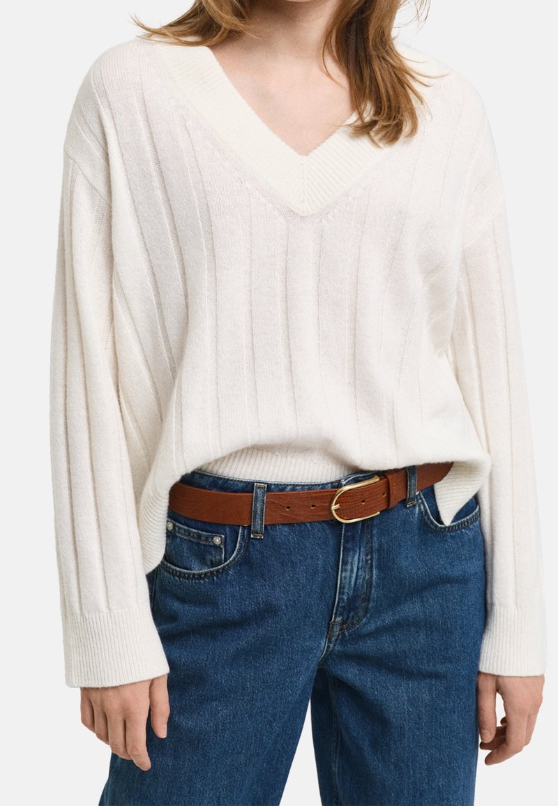 Pull côtelé crème avec un col en V et des manches oversize, associé à un jean en denim bleu et une ceinture en cuir marron.