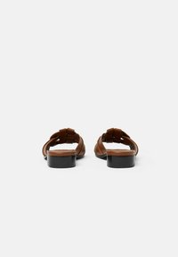 Sandali in pelle marrone con tacco basso nero a blocco, caratterizzati da un design intrecciato sulle cinghie superiori e una soletta liscia.