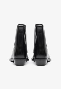Botines negros de cuero con textura suave, puntera redondeada y tacón bajo apilado. Detalle lateral elástico para facilitar el uso.