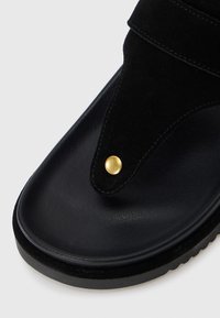 Sandali neri con una soletta in pelle opaca, tomaia in suede dalla forma triangolare distintiva e dettagli con borchie dorate.