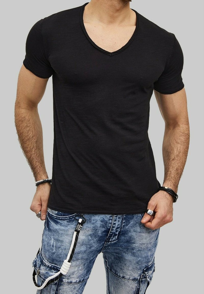 T-shirt noir à manches courtes et col en V, design ajusté, texture lisse. Porté avec un jean cargo bleu délavé comportant des accessoires et des détails contrastants.