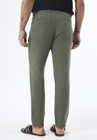 Olive green, lightweight pants with a textured fabric, slim fit, and slit pockets at the back. Worn with black sandals.
