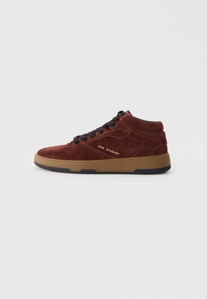 High-top sneakers made of rust-colored suede with black laces, a tan rubber sole, and gold "CPH STUDIOS" branding on the side.