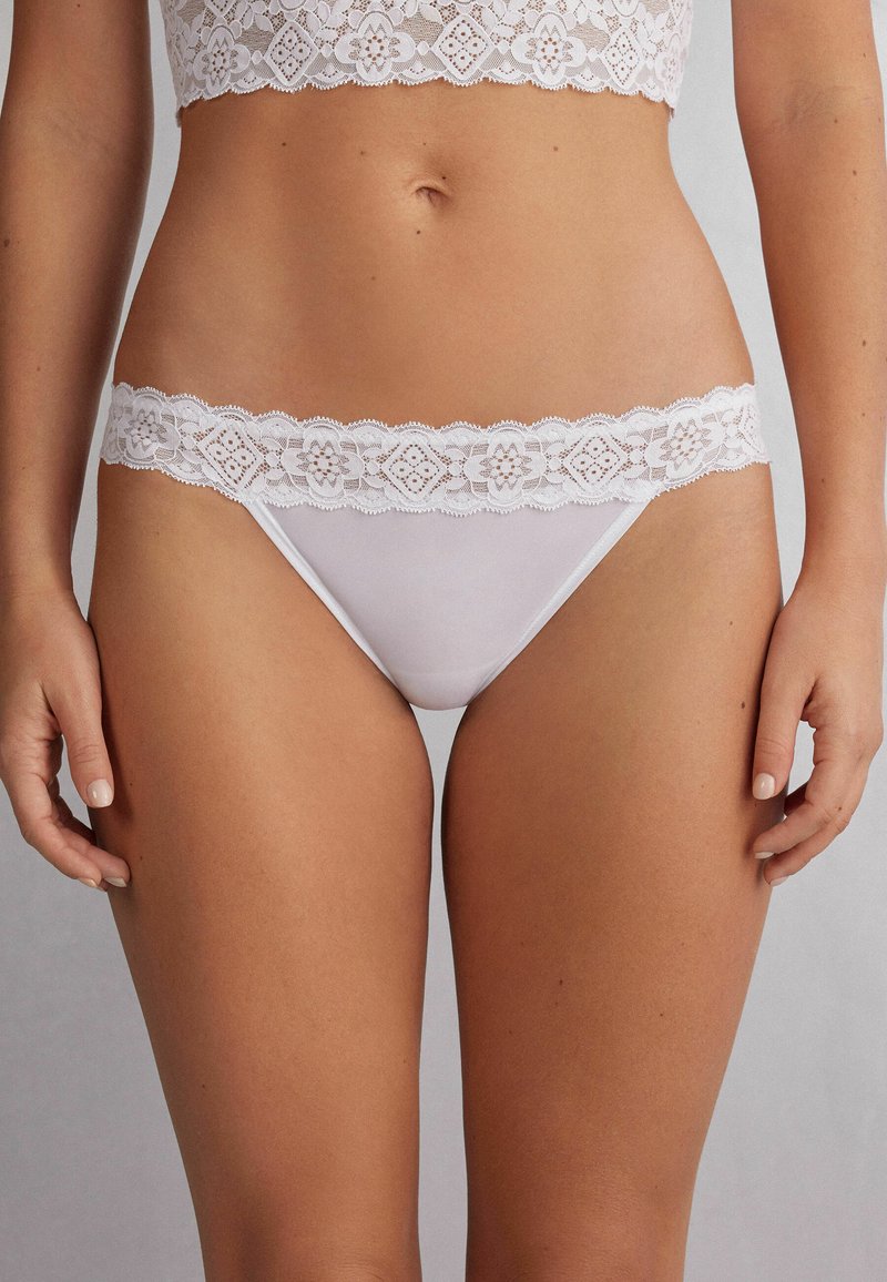 Ensemble bralette et string en dentelle blanche, avec une finition en dentelle florale, un micro-tissu sans couture et un délicat bord festonné sur la taille.