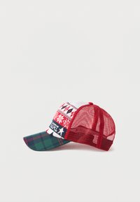 Gorra de malla roja con parte frontal blanca que presenta patrones de copos de nieve y triángulos. Visera de cuadros verdes y acento lateral con etiqueta "GIRL". El panel frontal tiene textura.