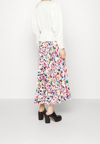 Blusa blanca de manga larga con cinturilla ceñida, combinada con una falda maxi de colores con plisados y un patrón abstracto multicolor. Mules de tacón bloque negros.