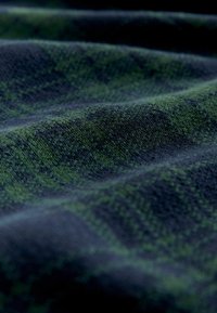 Gewebter Stoff mit einem dunkelblauen Grund und einem karierten grünen Muster, das eine weiche Textur und einen leichten Glanz zeigt.