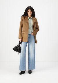 Brown suede blazer, light green shirt, wide-leg light blue jeans, black handbag with floral pattern, and black wedge boots.
