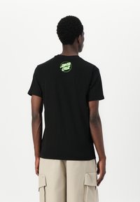 Sort bomulds T-shirt med korte ærmer, der har et cirkulært grønt "Santa Cruz" grafik på den øverste ryg. Enkel, afslappet design.