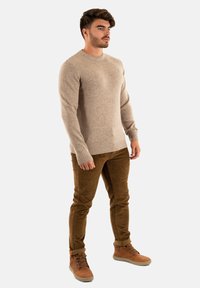 Pull en tricot beige clair avec un col rond, des poignets et un ourlet côtelés ; associé à un pantalon en velours côtelé marron et des bottes marron.