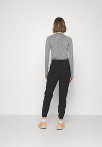 Cămașă sportivă gri cu mânecă lungă și un model texturat, asortată cu pantaloni negri tapered cu manșete elastice și accente reflectorizante.