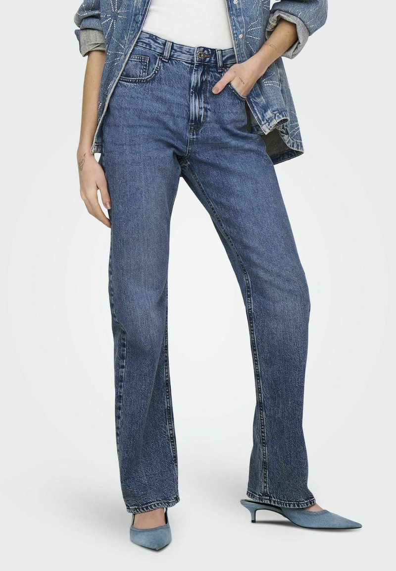 Jeans de mezclilla azul con campana y acabado desgastado, diseño de cinco bolsillos y detalles de costura visibles. Combinados con zapatos puntiagudos de color azul claro.