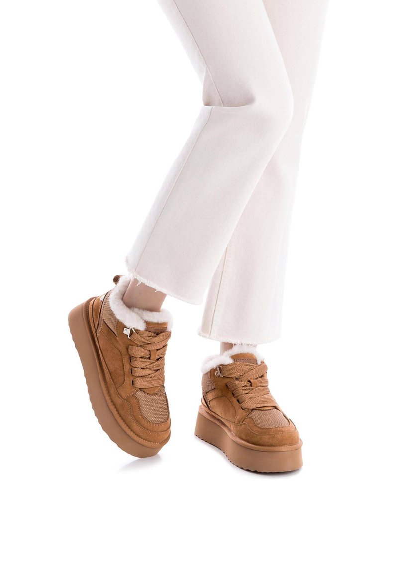 Zapatillas altas marrones con malla y ante, que cuentan con un cuello forrado de piel, suela gruesa y cordones planos. Combinadas con jeans blancos deshilachados.